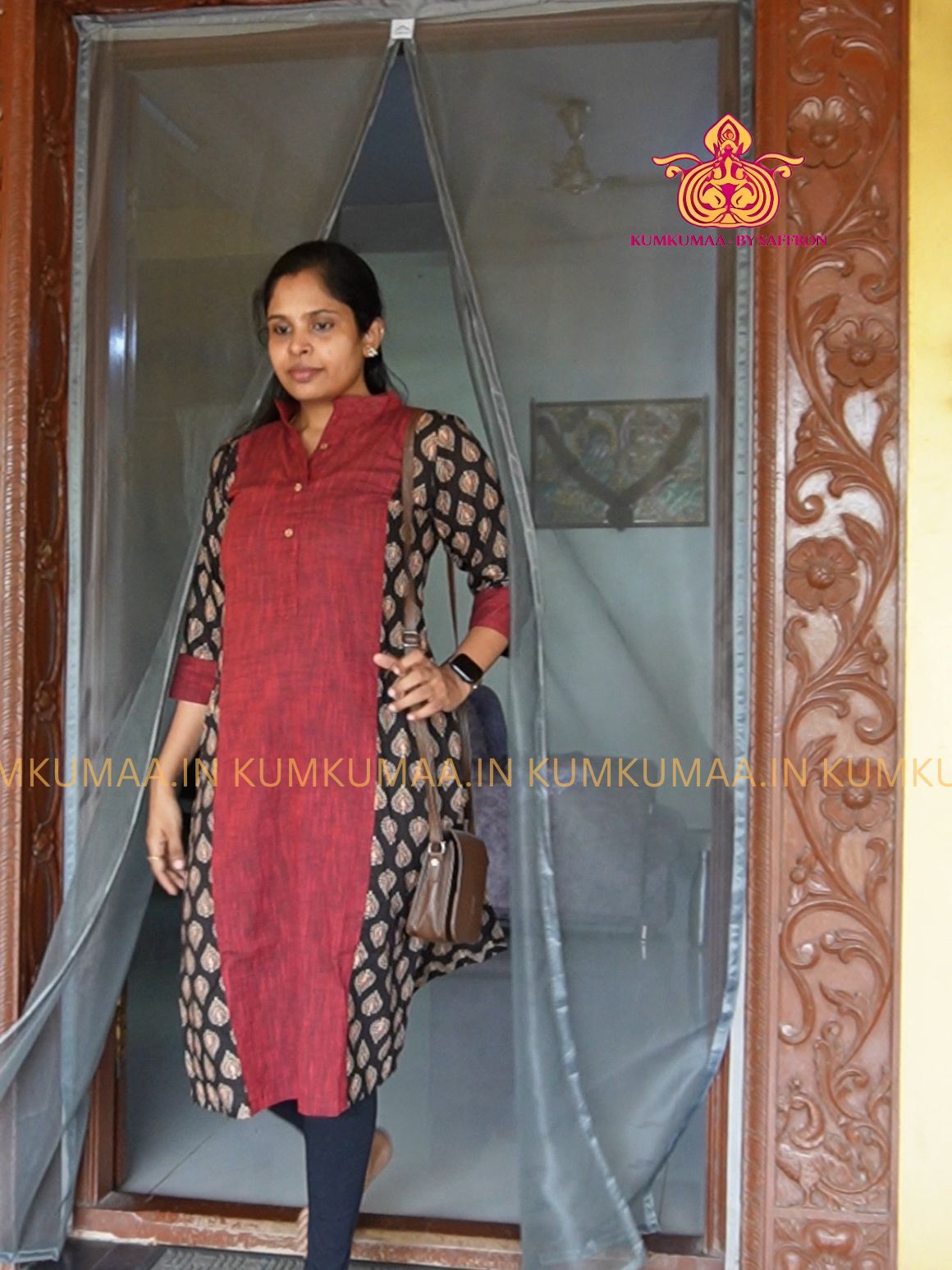 Woman standing in a doorway wearing a red and black traditional outfit, with a decorative logo in the corner.